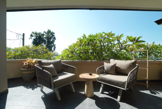 Hotel room balcony with franjipani trees and blue skies in the background.